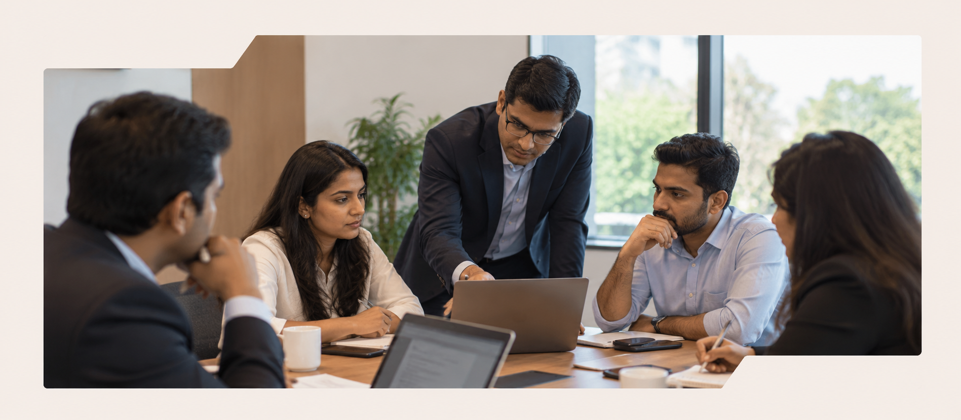 A colleague standing at the head of a meeting table, walking four seated advisors through an analysis on a laptop.